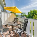 Terrasse mit Tisch, Stühlen und gelbem Sonnenschirm. Blick auf grüne Bäume und einen Nachbarhof.