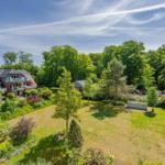 Haus mit Garten und Bäumen unter blauem Himmel.