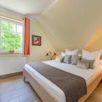 Schlafzimmer mit Dachschrägen, Bett, Nachttisch, TV und Fenster mit Blick auf Grün.