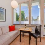 Wohnbereich mit Sofa, Tisch und Stuhl. Große Fenster mit Blick auf Balkon und Umgebung.