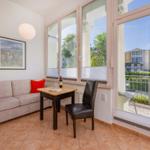 Wohnzimmer mit Sofa, Tisch und Stuhl. Balkon mit Blick auf Grünflächen.