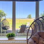 Rattan-Schaukelstühle vor großem Fenster mit Blick auf Garten und Landschaft.