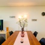 Esszimmer mit Holztisch, Stühlen und Blumenvase. Wanddekoration und Uhr sichtbar.