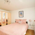 Schlafzimmer mit Bett, Schrank und Nachttisch. Wandbild und Blumen.