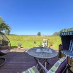 Terrasse mit Hängesessel, Tisch und Strandkorb. Blick auf grünes Feld unter blauem Himmel.