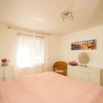 Schlafzimmer mit Bett, Schrank und Stuhl. Fenster mit Vorhängen und Wandbild.