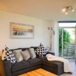Ein Wohnzimmer mit einem grauen Sofa, Kissen und einer weißen Decke. Eine Glastür führt auf eine Terrasse.