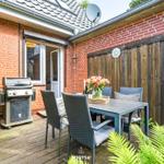 Terrasse mit Grill, Tisch und Stühlen. Roter Backsteinbau mit Holztür.