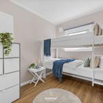 Schlafzimmer mit Doppelstockbett, Schrank und Nachttisch. Holzboden und Fenster sichtbar.