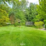 Großer Garten mit Trampolin, Grillplatz und umliegenden Bäumen.