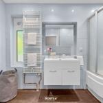 Badezimmer mit Dusche, Waschbecken und Heizung. Fenster und Handtuchhalter sichtbar.