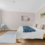 Schlafzimmer mit Bett, Stuhl und Wandbild. Holzboden und Fenster.