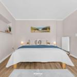 Schlafzimmer mit Bett, Wandbild und Holzboden. Tür führt in einen anderen Raum.