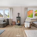 Wohnzimmer mit Kamin, Sofa und Sessel vor Fenstern mit Blick auf Garten.