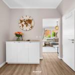 Eingangsbereich mit weißen Schränken, Weltuhr und Blumen. Durchgang zum Wohnzimmer mit Sofa.