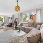 Wohnzimmer mit Sofa, Couchtisch und Fenstern. Holzboden und Deckenleuchte.