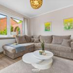 Wohnzimmer mit Ecksofa, runden Tisch und Fenster zum Garten.