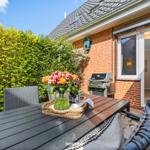 Terrasse mit Tisch, Stühlen und Grill. Blick in die Küche. Grüner Heckenzaun.