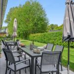 Terrasse mit Tisch, Stühlen und Sonnenschirmen. Grünflächen und Bäume im Hintergrund.