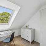 Dachgeschosszimmer mit Schreibtisch, Kleiderschrank und Dachfenster mit Blick auf Bäume.
