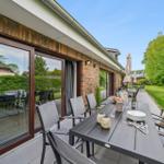 Terrasse mit Tisch, Stühlen und Sonnenschirmen neben grünem Garten.