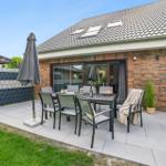 Terrasse mit Tisch, Stühlen und Schirm. Hintergrund: Haus mit Glasfront und Dachfenstern.