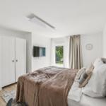 Schlafzimmer mit Bett, Kleiderschrank, Fernseher und Fenster mit Blick auf Garten.