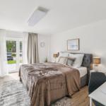 Schlafzimmer mit Bett, Schreibtisch und Glasfront zur Terrasse.