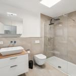 Badezimmer mit Dusche, Waschbecken und Toilette. Fliesenwand und Spiegelschrank.