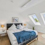 Schlafzimmer mit Dachfenstern, Bett, Nachttischen und Pflanzen.