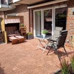 Terrasse mit Liegestuhl, Tisch und Stühlen. Pflanzen und Ziegelsteinbelag.