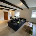 Wohnzimmer mit Sofa, Couchtisch und Essbereich unter Balkendecke.