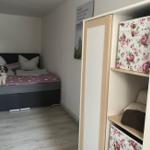 Schlafzimmer mit Bett, kleinem Hund und Kleiderschrank mit Blumenmuster.