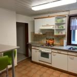 Küche mit weißen Schränken, Arbeitsplatte und Fenster mit Vorhang.