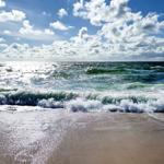 Wellen brechen an einem sandigen Strand unter einem bewölkten Himmel.