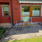 Außenbereich mit Tisch und zwei Stühlen vor rotem Haus mit Fenstern.