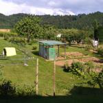 Garten mit Gemüsebeeten, Zaun und Blick auf bewaldete Hügel.