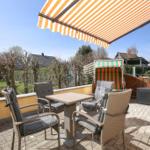 Terrasse mit Sitzgruppe, Sonnenschutz und Blick auf Garten und Nachbarhäuser.