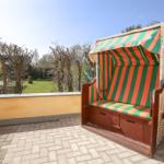 Terrasse mit Strandkorb in grün-orange Streifen, Blick auf Garten und Bäume.