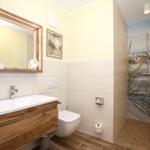 Badezimmer mit Dusche, Waschbecken und Toilette. Duschwand zeigt Strandmotiv.