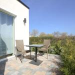 Terrasse mit Tisch und zwei Stühlen vor einer Glasfront.