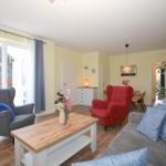 Wohnzimmer mit Sofa, Sessel und Esstisch. Große Fenster und Pflanzen.