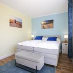 Schlafzimmer mit Bett, Nachttisch und Wandbildern. Fenster mit Blumen.
