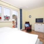 Schlafzimmer mit Bett, TV-Schrank, Sessel und Fenster zur Terrasse.