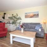 Wohnzimmer mit Sofa, roter Sessel und Küchenbereich
