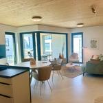 Wohn- und Essbereich mit Holzdecke, Sofa, Tisch und Fenstern zum Balkon.