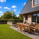 Terrasse mit Holztisch und Stühlen vor einem Backsteinhaus mit Garten.