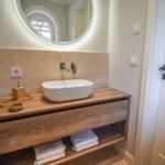 Waschbecken auf Holzkonsole mit Spiegelschrank und Handtuchregal.