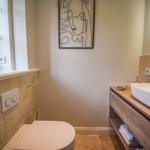Badezimmer mit Waschbecken, Toilette und Fenster mit Pflanze.