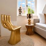 Ein goldener Handsessel steht neben einem Sofa mit Kissen und einem Tisch mit Lampe.